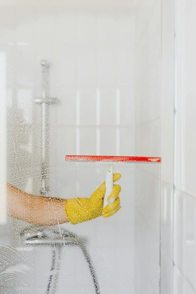Handschuhhand zieht Glas-Duschwand mit Abzieher ab
